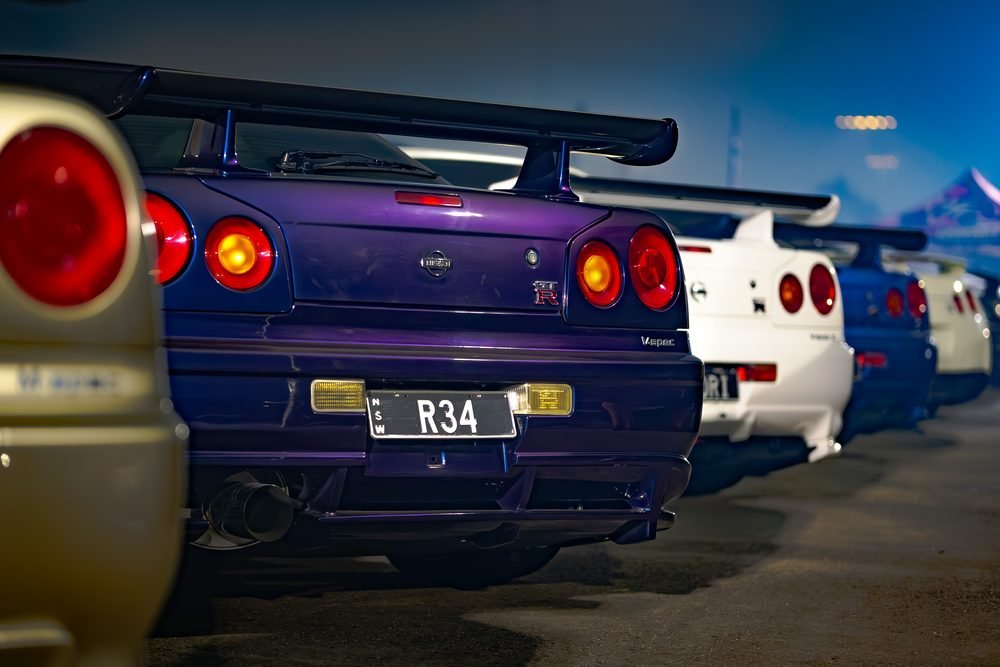 Midnight purple Nissan Skyline R34 GT-R V-Spec at the head of a line of R34s at dusk