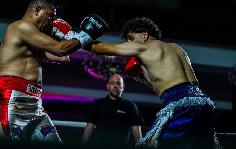 Two boxers trading punches mid-round with the referee watching behind them