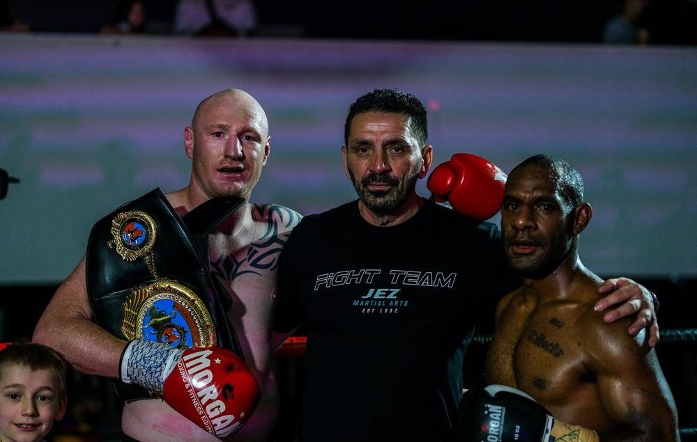 Winning boxer with the championship belt beside his opponent and their coach in the ring