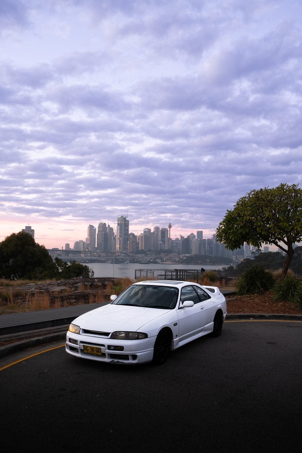 White Nissan Skyline GTS against the Sydney skyline in the last of the light