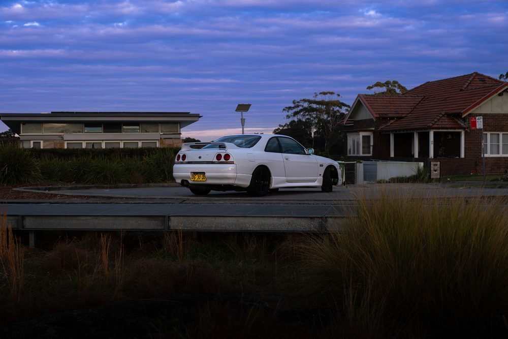 Nissan Skyline GTS photographed against the Sydney city skyline and Harbour Bridge at sunset (frame 11 of 12)