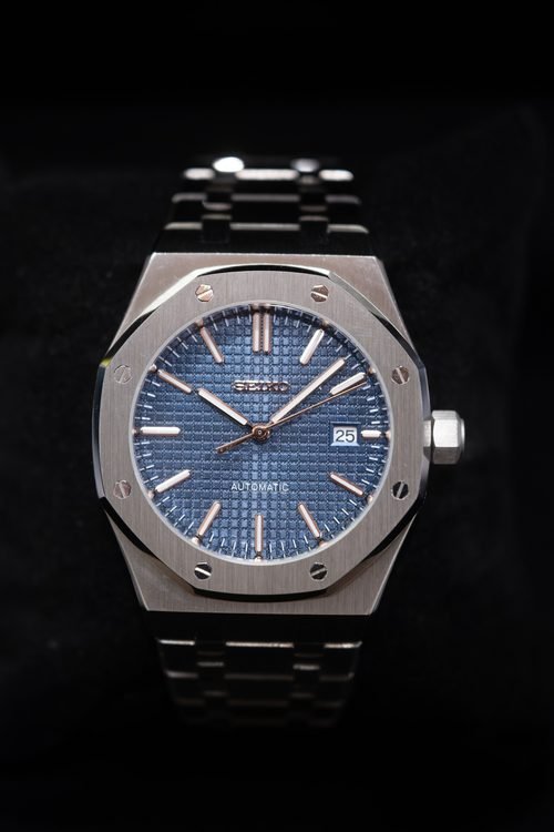 A steel automatic watch with a blue dial, shot on black