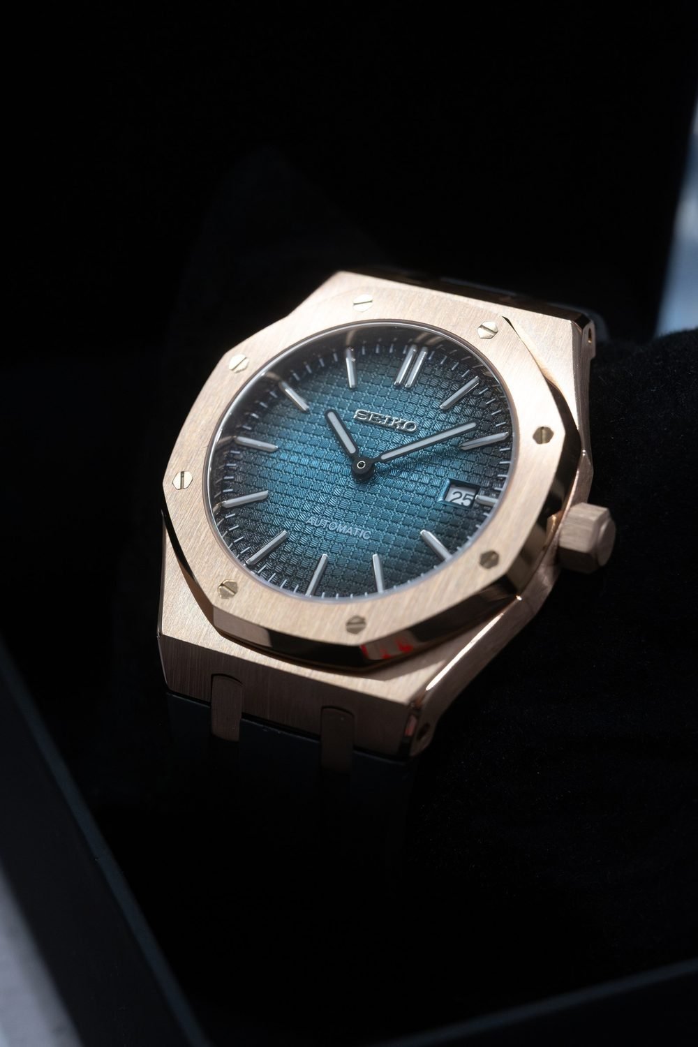 Rose gold sports watch with a teal tapisserie dial on a rubber strap