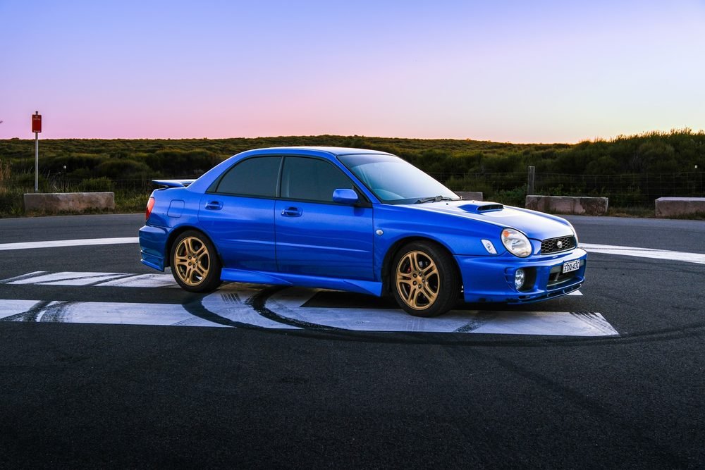 Blue Subaru Impreza WRX STI on gold wheels at a coastal roundabout during blue hour